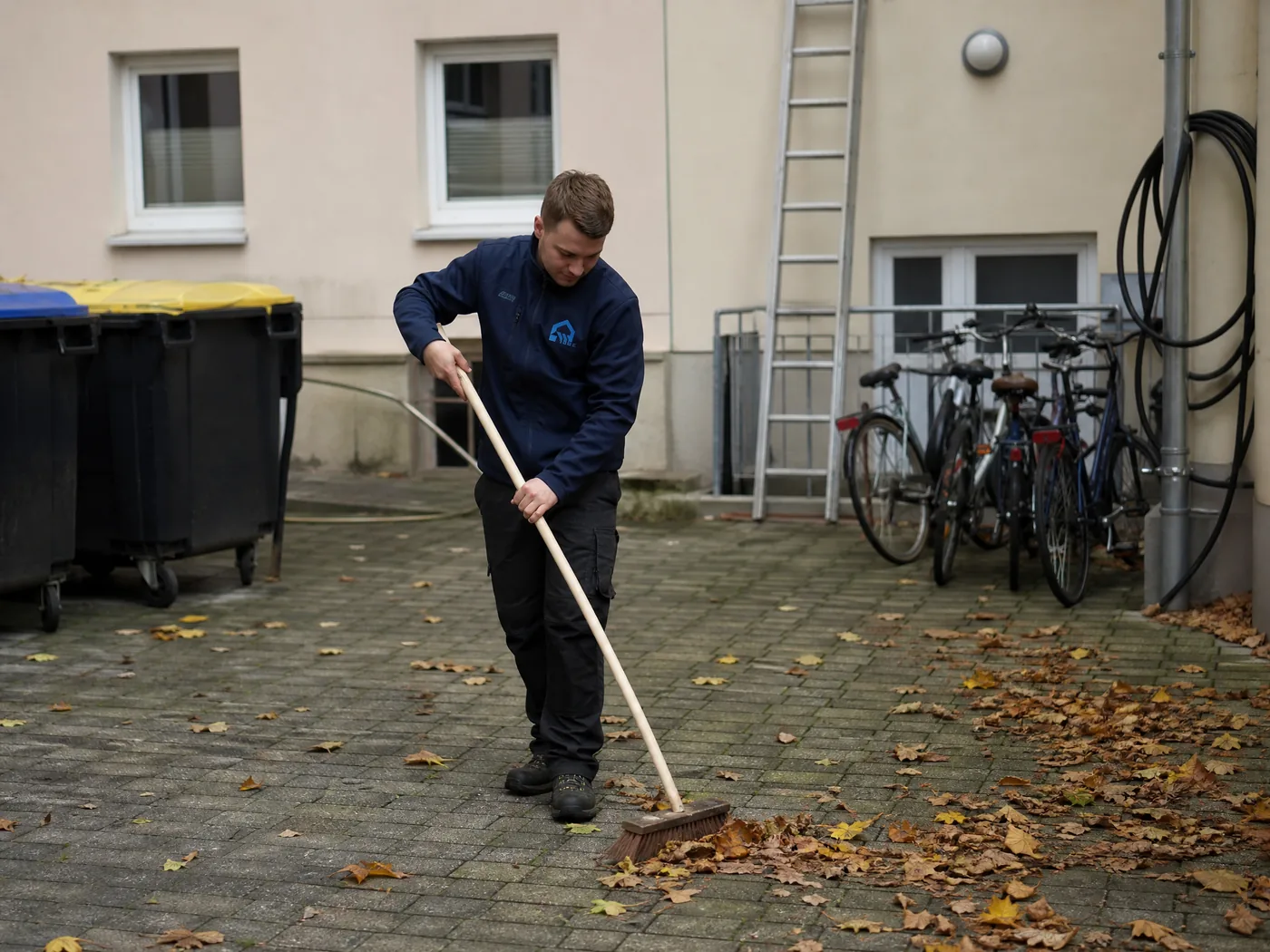 Hausmeister von S&E Gebäudereinigung kehrt Laub im Innenhof einer Wohnanlage in Dresden