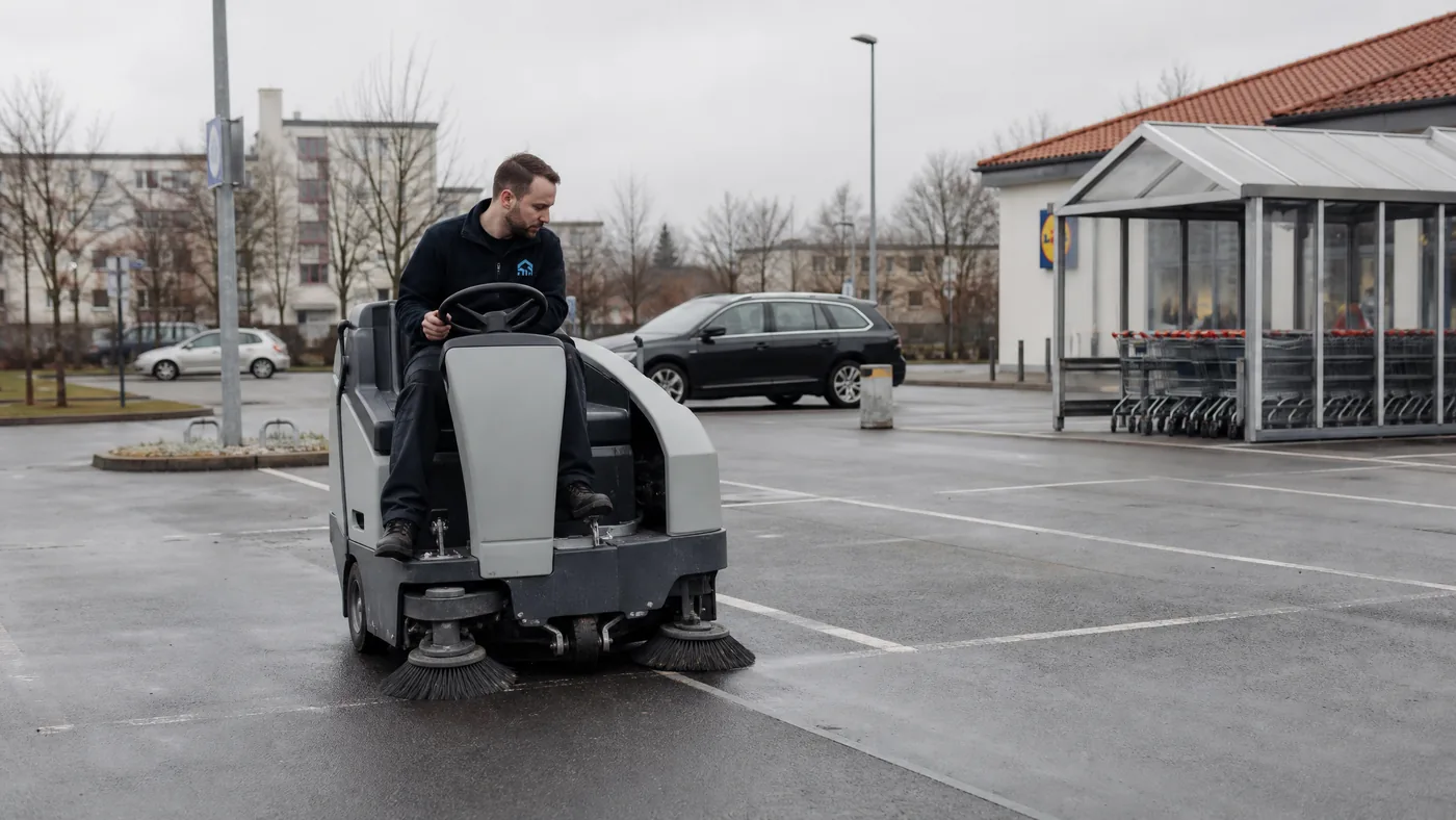 Mitarbeiter von S&E Gebäudereinigung reinigt mit einer Kehrmaschine den Parkplatz eines Supermarkts in Dresden